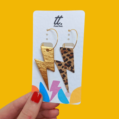 Leopard print and gold lightning bolt earrings on a branded card against a yellow background