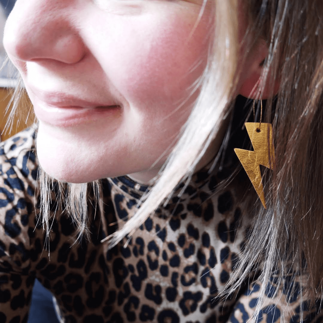 Close-up of a person wearing a gold lightning bolt earring with a leopard print top.