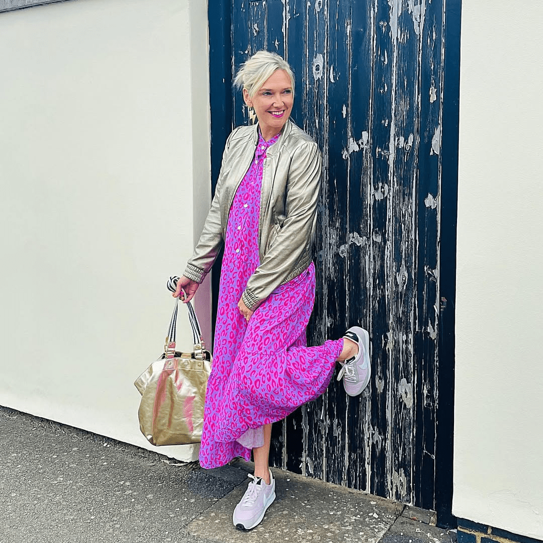 Woman in a pink dress and green jacket posing against a textured wall.
