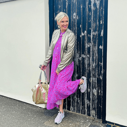 Woman in a pink dress and green jacket posing against a textured wall.