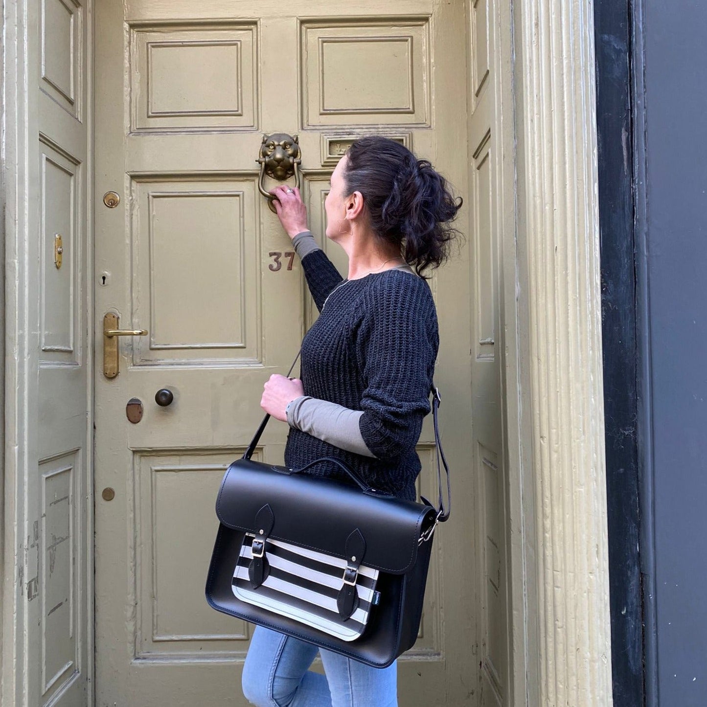 Woman with a black satchel bag standing in front of a door