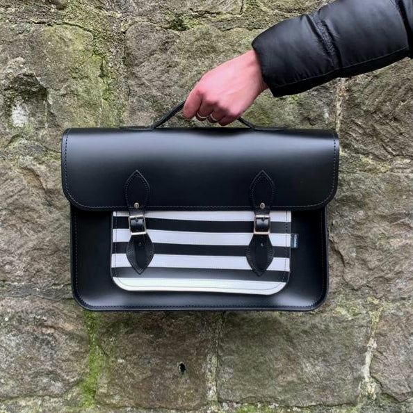 Black satchel with a striped pattern held against a stone wall