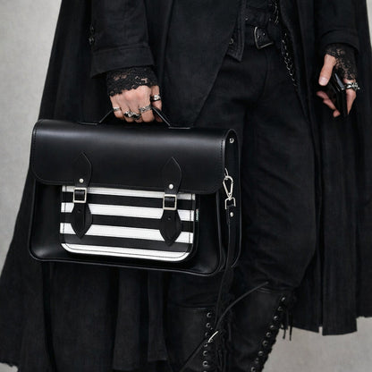 Person holding a black satchel with a striped pattern, wearing a dark coat and boots.