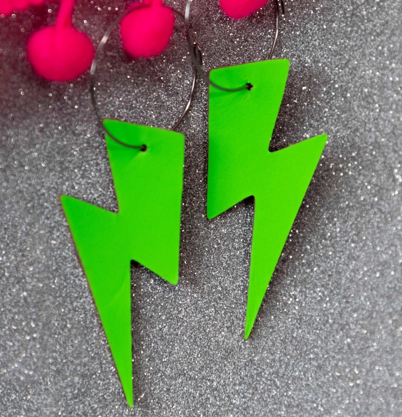Green lightning bolt earrings on a glittery gray background