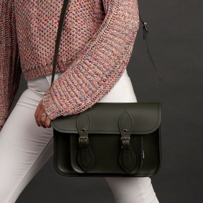 Person holding a black leather satchel bag against a dark background