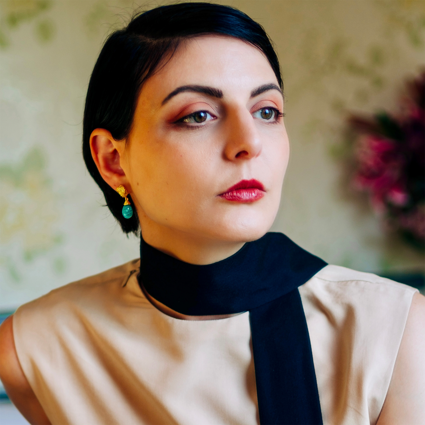 Woman wearing a beige top with a black scarf, looking directly at the camera.