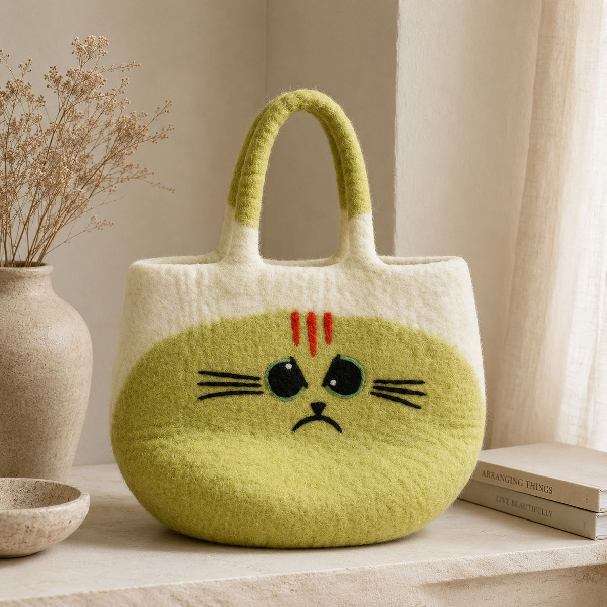 Large Grumpy Cat Felted Bag on a pale shelf beside a vase of dried flowers and a stack of books