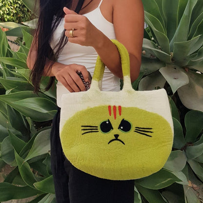 Woman carrying the Large Grumpy Cat Felted Bag by its handle in front of green plants