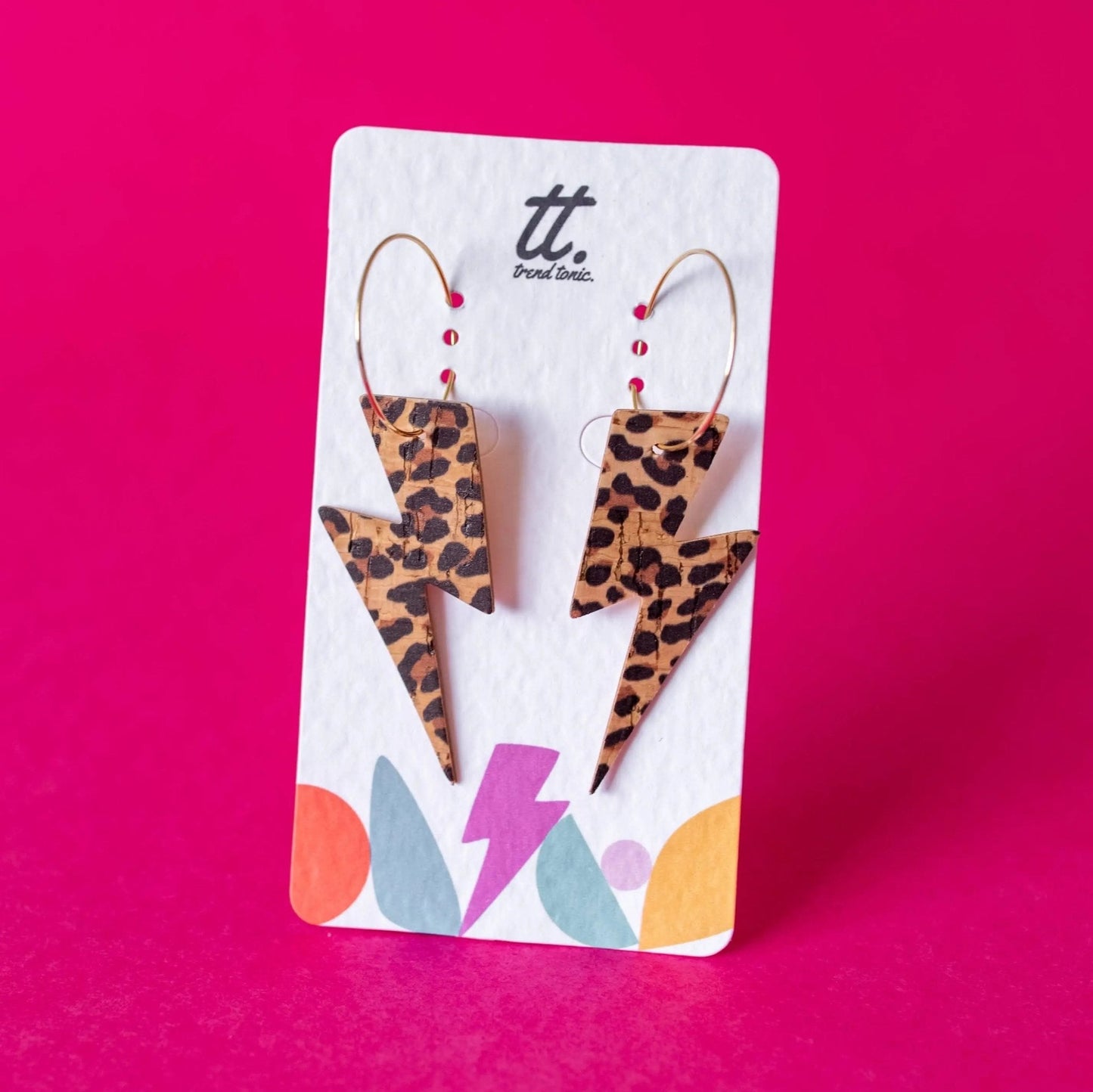 Leopard print lightning bolt earrings on a branded card against a pink background