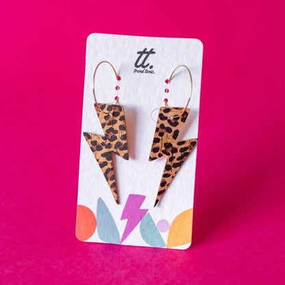 Leopard print lightning bolt earrings on a branded card against a pink background