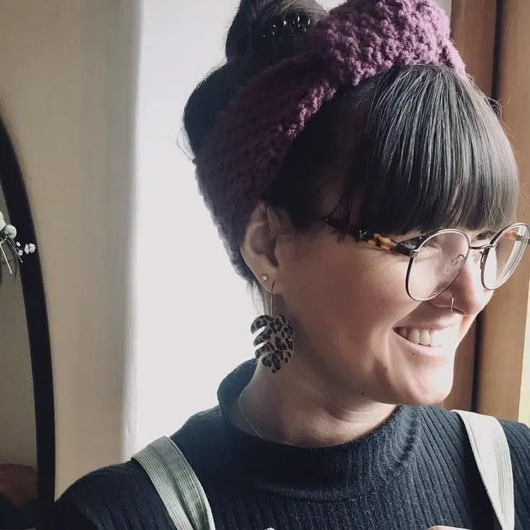 Person wearing a purple knitted headband and glasses, smiling.