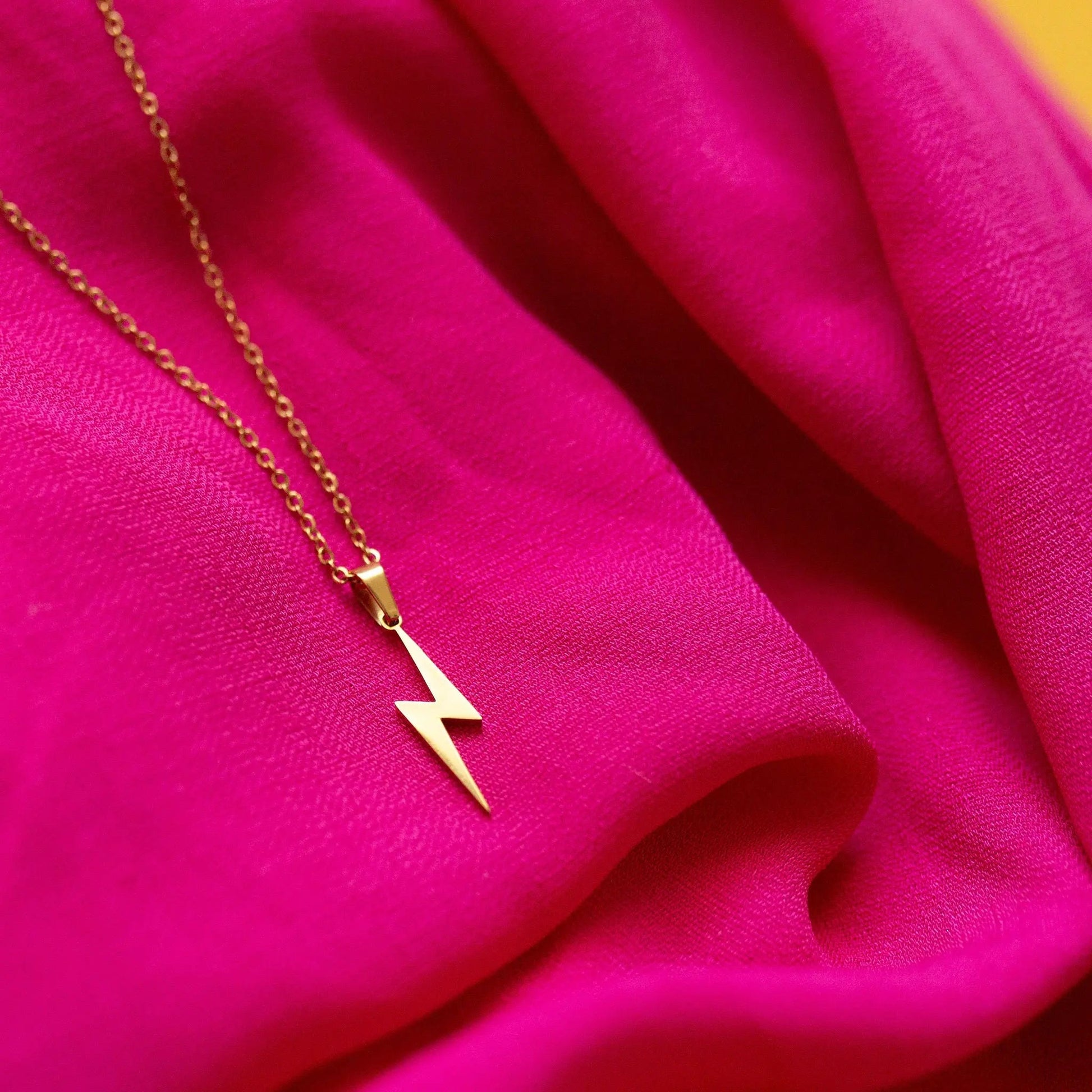 Gold lightning bolt necklace on a pink fabric background