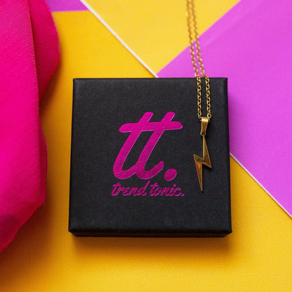 Gold necklace with a lightning bolt pendant on a Trendylicious box against a colorful background