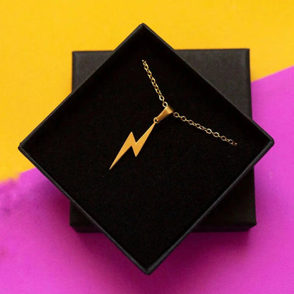 Gold necklace with a lightning bolt pendant on a black box against a yellow and purple background