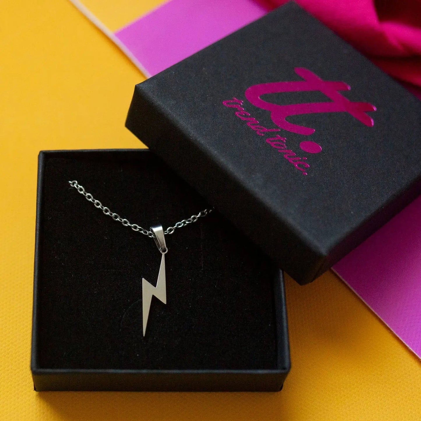 Silver lightning bolt necklace in a black box with a visible brand logo on a colorful background