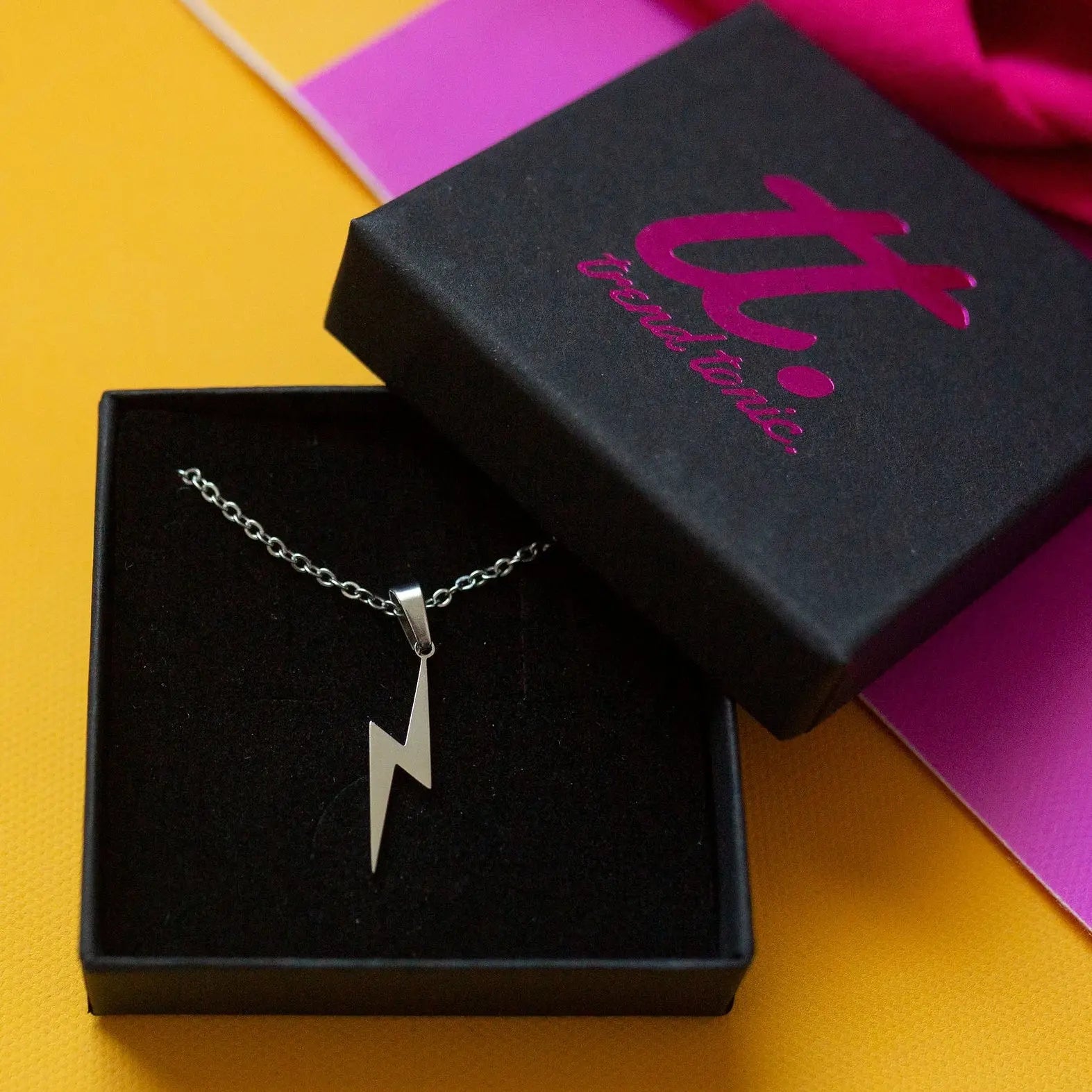 Silver lightning bolt necklace in a black box with a visible brand logo on a colorful background