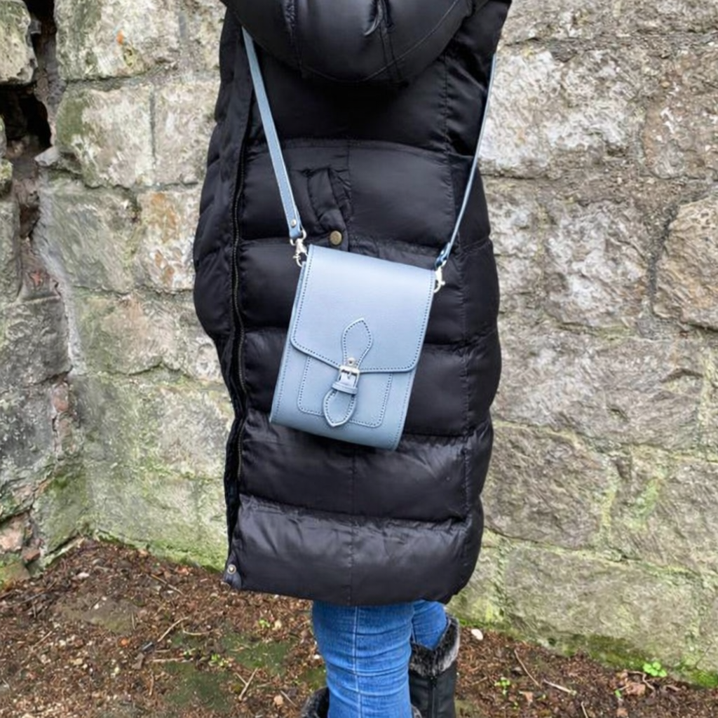 Person wearing a black puffer coat with a light blue crossbody bag against a stone wall.