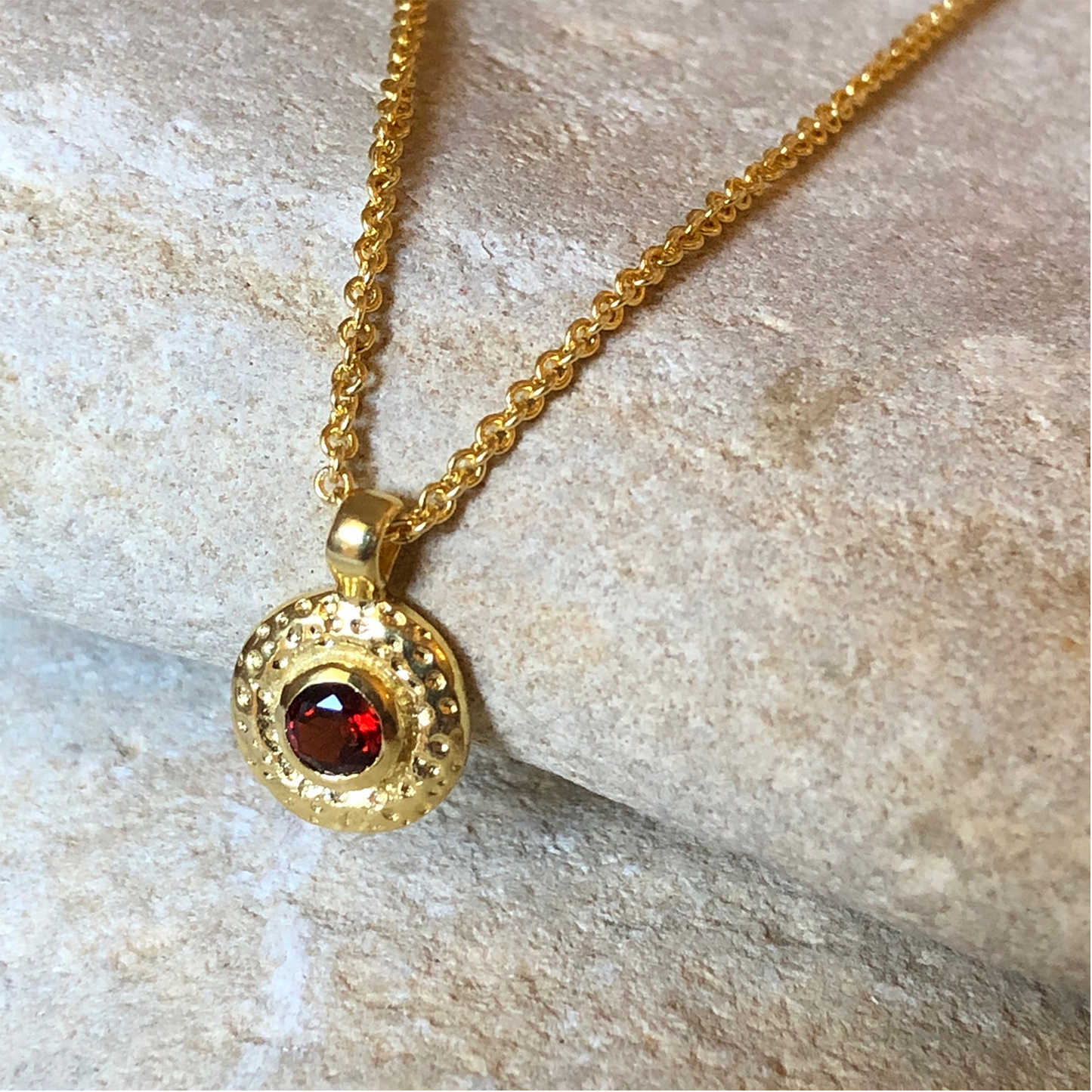 Gold necklace with a red gemstone pendant on a stone surface