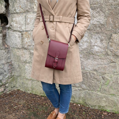 Person wearing a beige coat with a burgundy handbag against a stone wall.