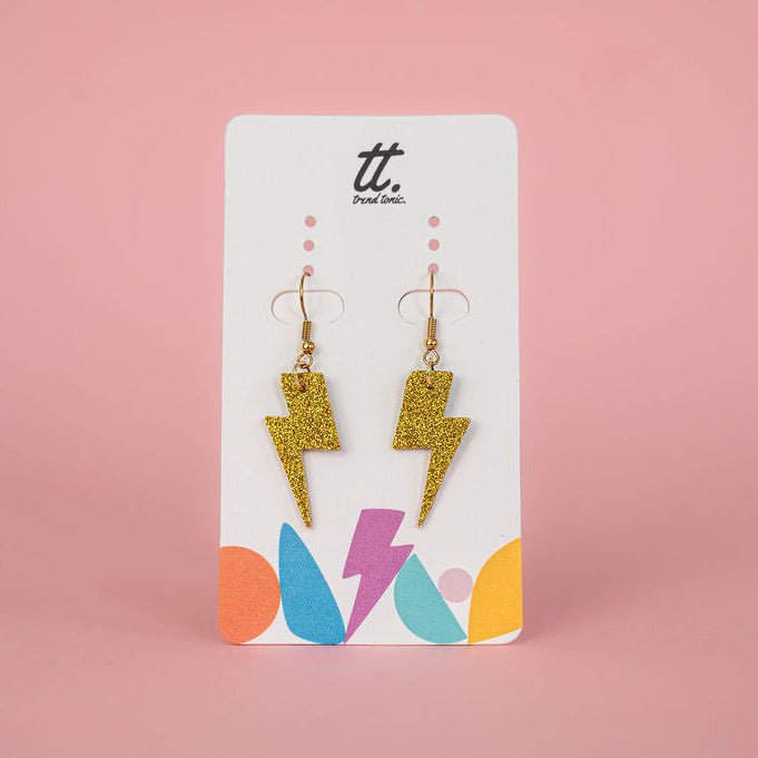 Gold glitter lightning bolt earrings on a branded card with a pink background