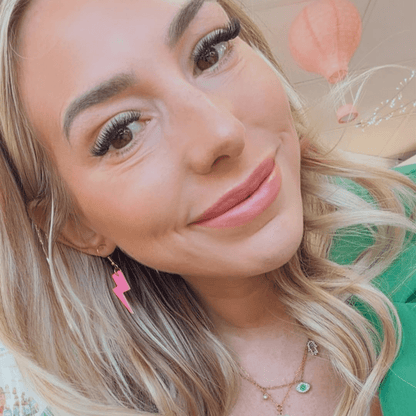 Close-up of a woman with blonde hair and pink earrings, wearing a green top.