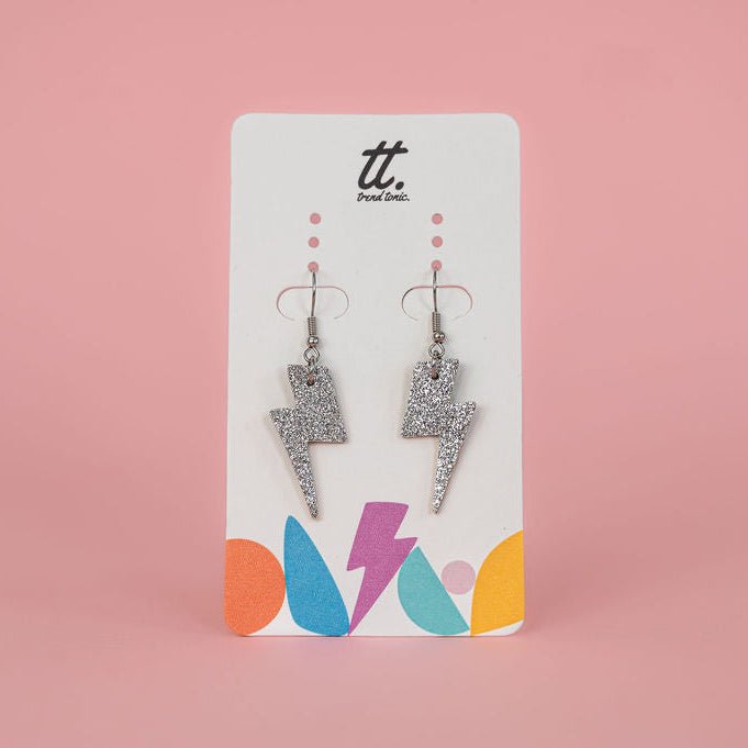 Pair of silver glittery lightning bolt earrings on a branded card against a pink background