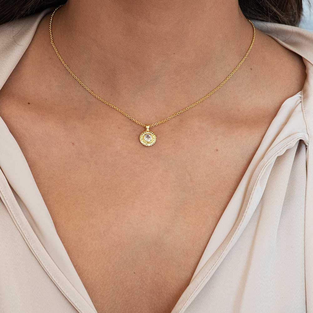 Gold necklace with a pendant on a person wearing a light-colored top.