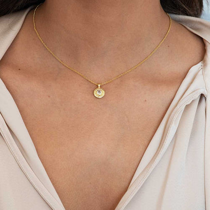 Gold necklace with a pendant on a person wearing a light-colored top.