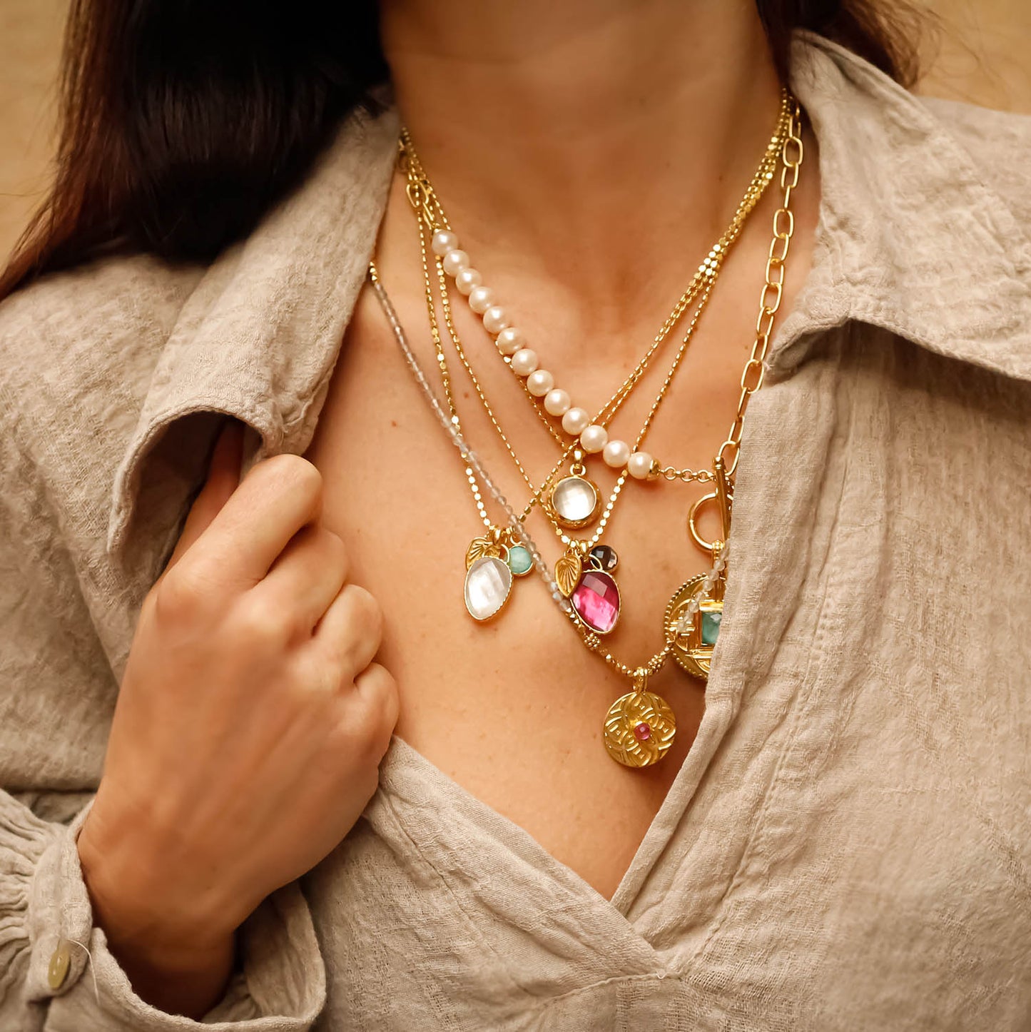 Close-up of a woman wearing multiple gold necklaces with various pendants.