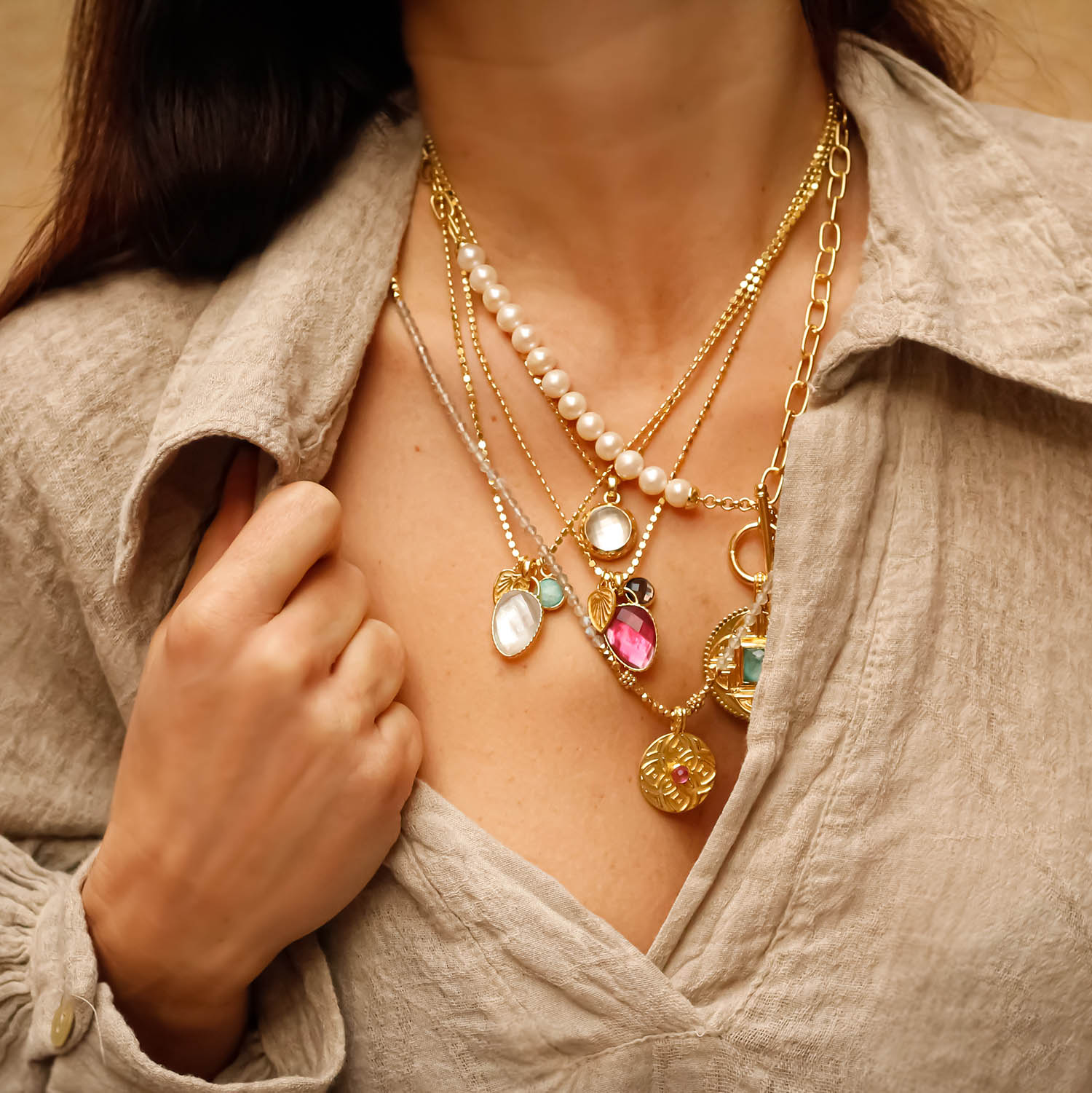 Close-up of a woman wearing multiple gold necklaces with various pendants.