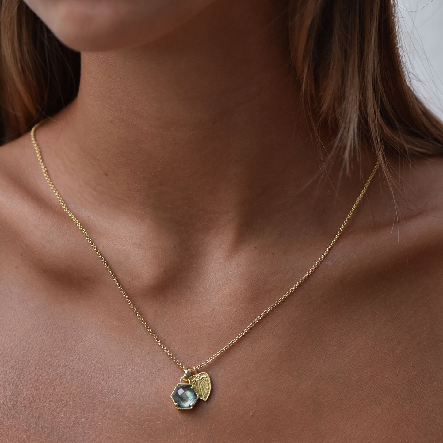 Gold necklace with a heart-shaped pendant featuring a green gemstone on a person's neck.