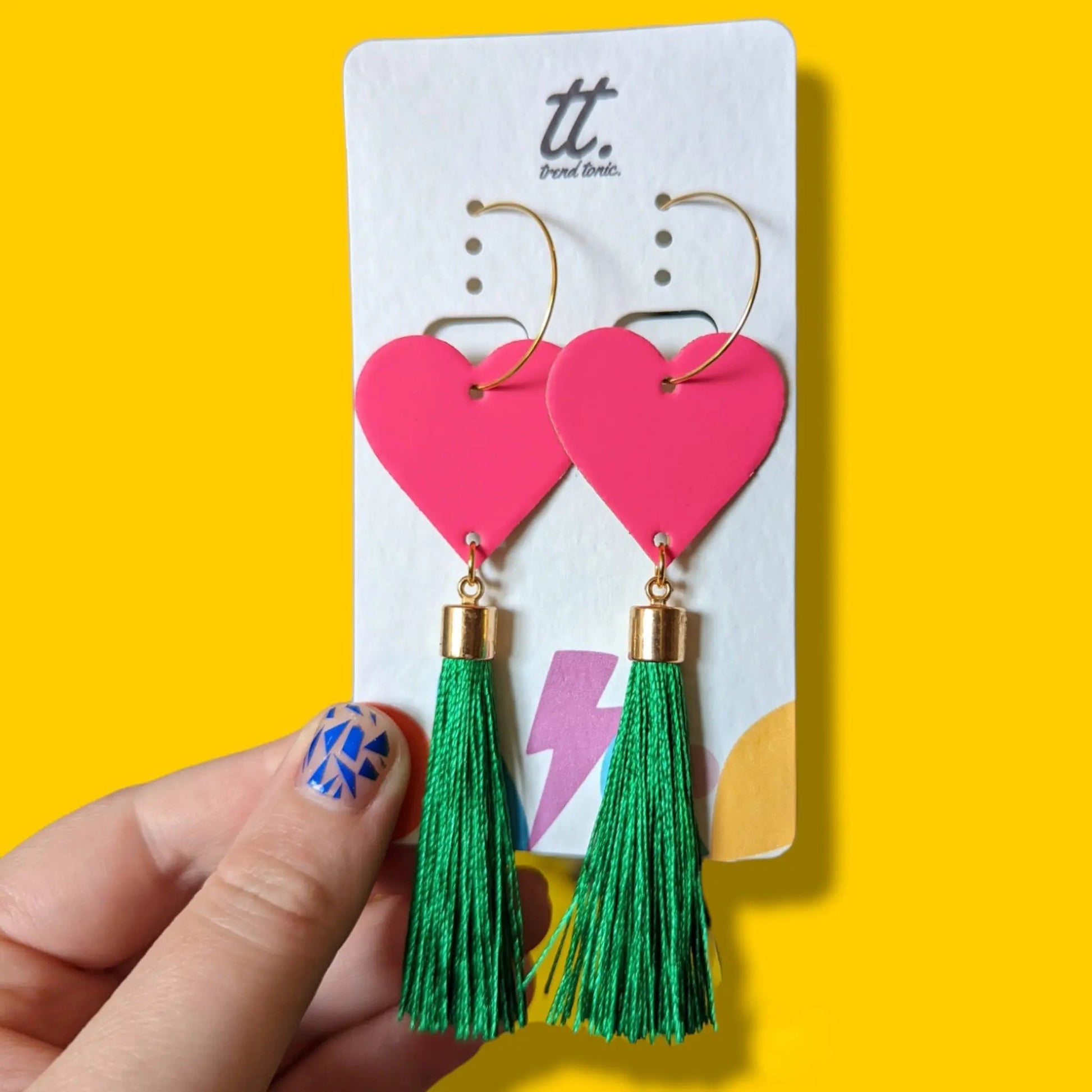 Heart-shaped earrings with green tassels on a yellow background