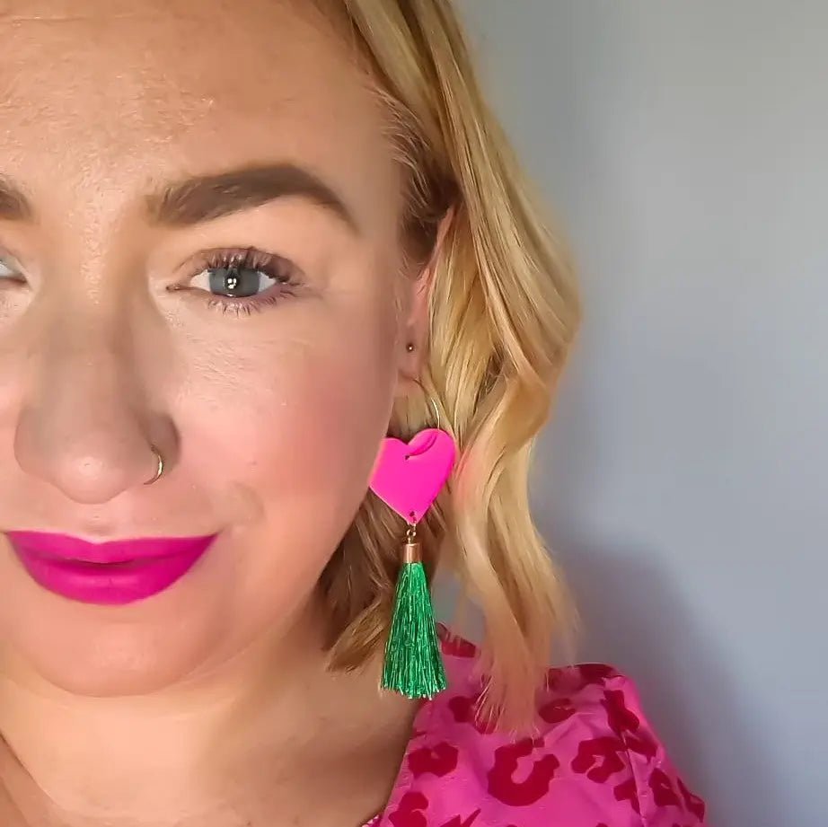Close-up of a person wearing a pink earring with a green tassel against a neutral background