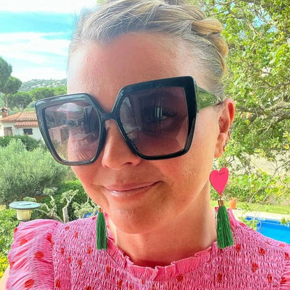 Woman wearing large sunglasses and pink top with green earrings outdoors