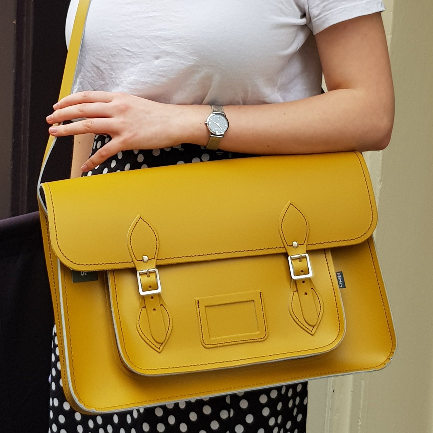 Yellow satchel bag held by a person wearing a white shirt and polka dot skirt.