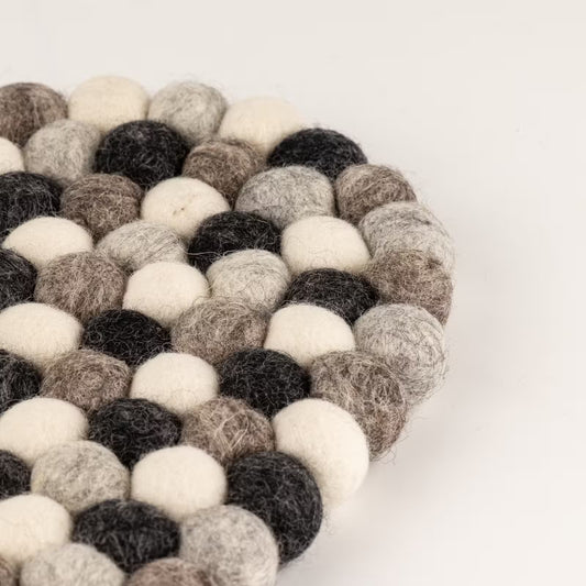 Close-up of the edge of the grey felt ball oval mat, showing charcoal, grey, taupe and cream wool balls