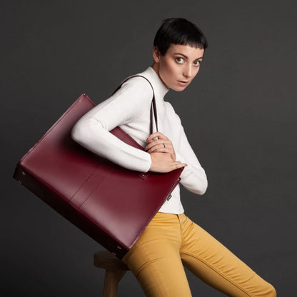 Woman holding a maroon briefcase against a dark background