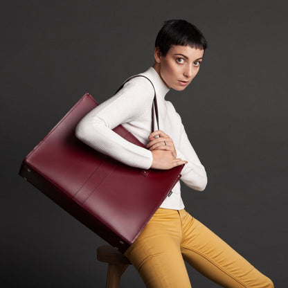 Woman holding a maroon leather briefcase against a dark background