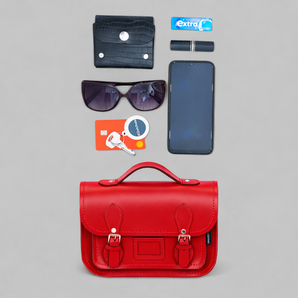 Red satchel bag with various items including a phone, wallet, sunglasses, and cards on a gray background.