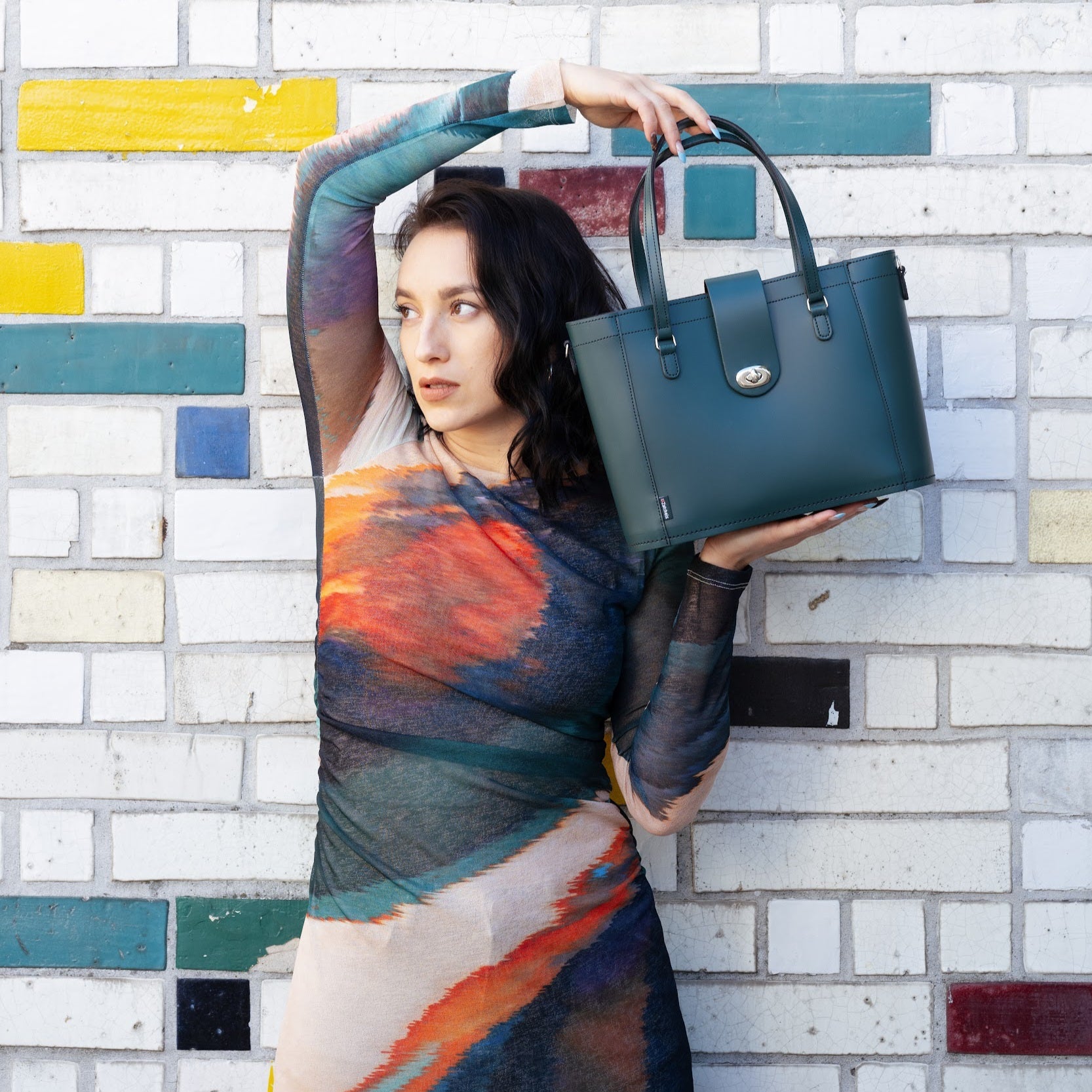 Woman holding a green handbag against a colorful brick wall.