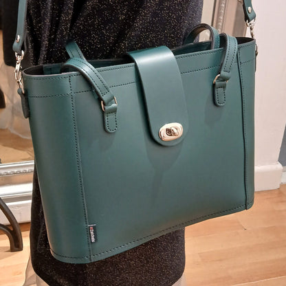 Green handbag with a gold clasp on a mannequin against a neutral background