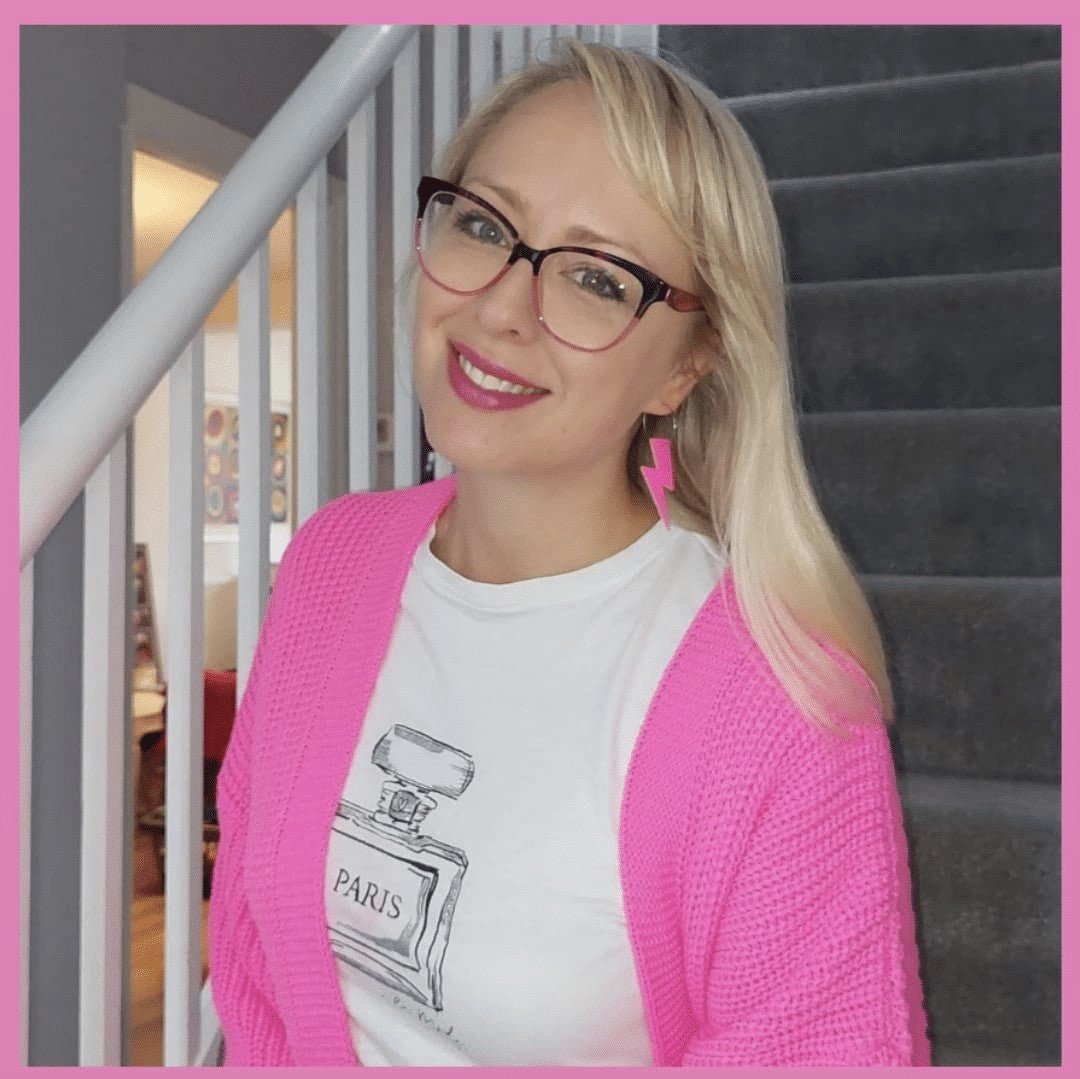 Woman wearing a pink cardigan and white shirt with a graphic design, standing indoors.