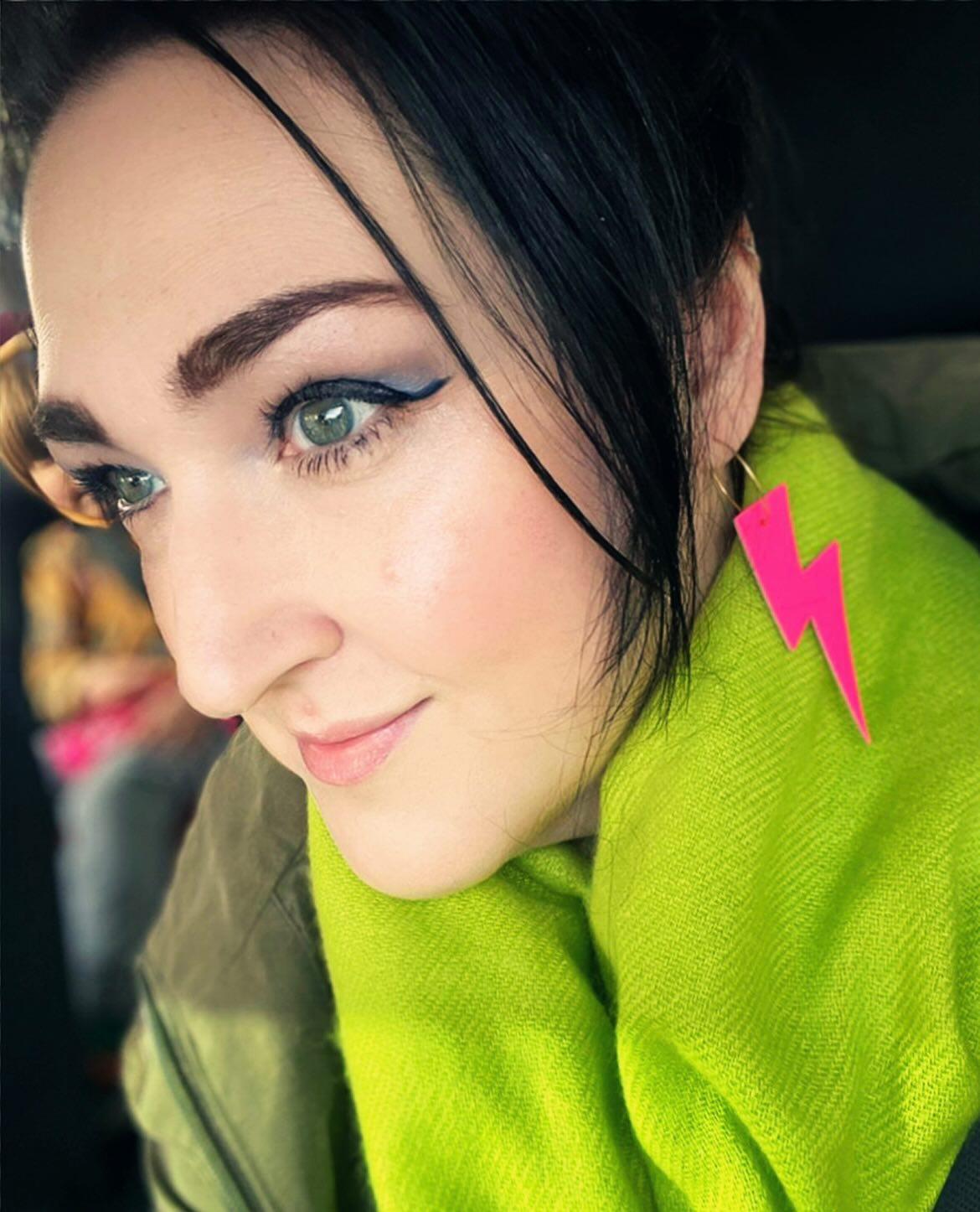 Person wearing a bright green jacket with a pink lightning bolt design, sitting in a vehicle.