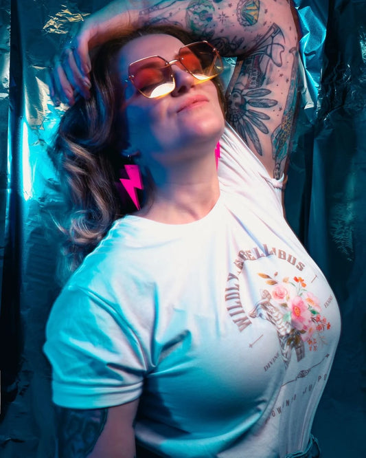 Person wearing a white t-shirt with colorful graphics and text, standing against a dark background.