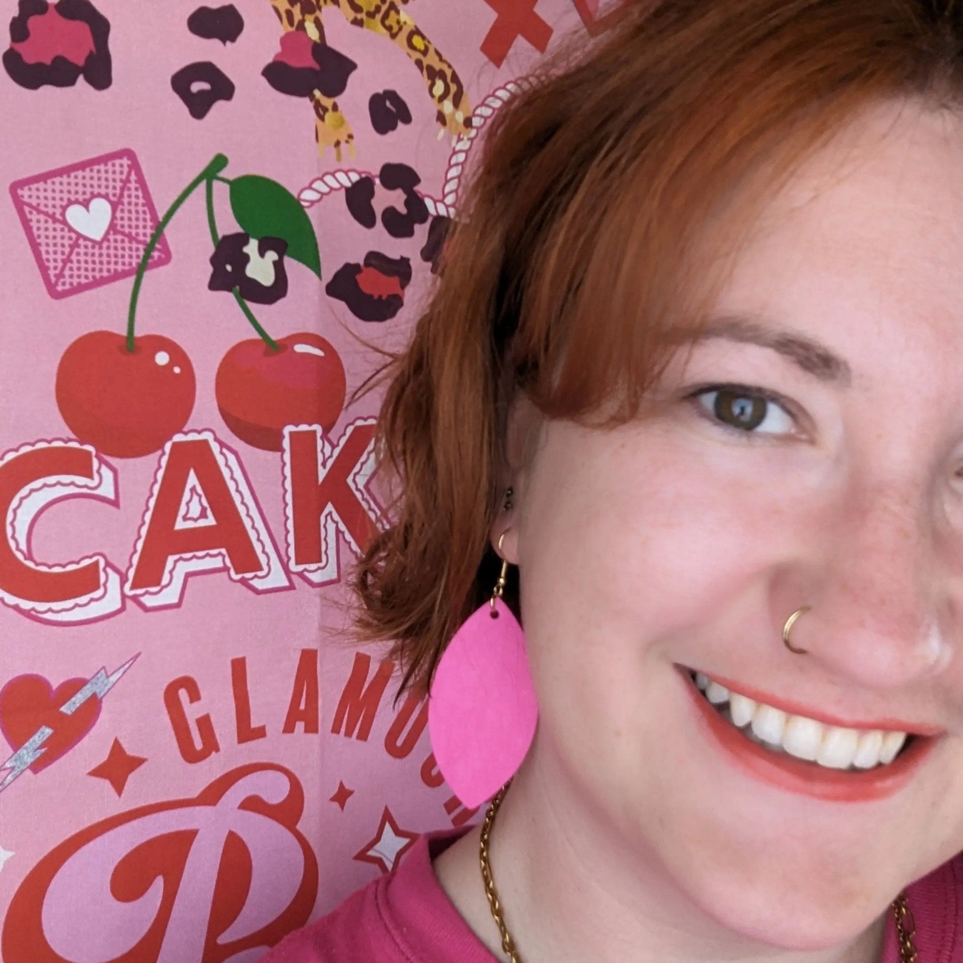 Person with red hair and pink earrings against a pink background with decorative text and graphics.