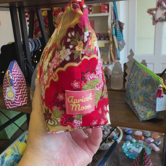 Hand turning the Isumi Red Japanese everyday pouch to show the print, zip and tassel in the Apricot Moon shop