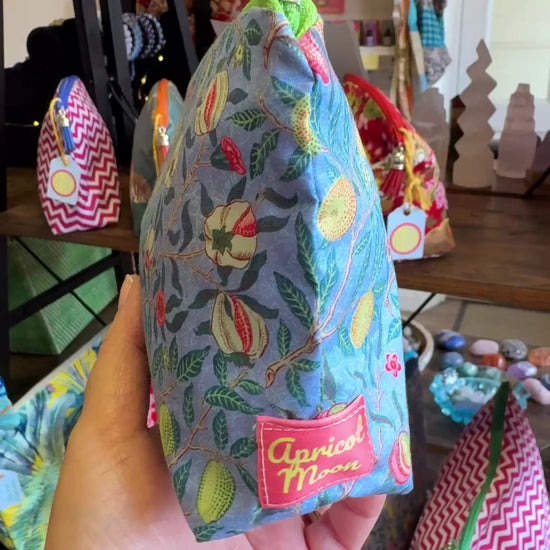 Hand turning the Garden Fruits everyday pouch to show the fruit print, zip and tassel in the Apricot Moon shop