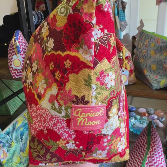 Hand turning the Isumi Red Japanese wash bag to show the print, zip and tassel in the Apricot Moon shop