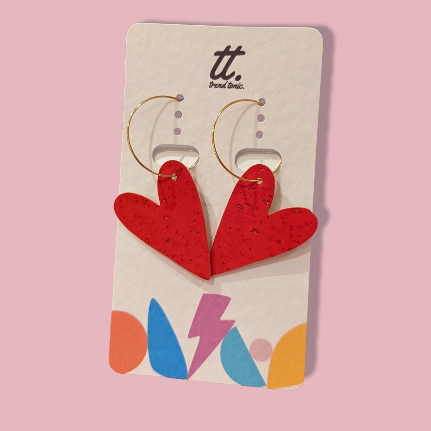 Red heart-shaped earrings on a branded card with a pink background