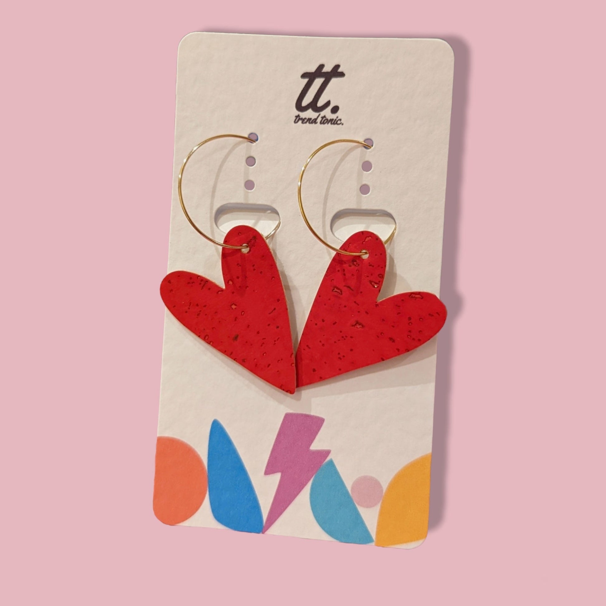 Red heart-shaped earrings on a branded card with a pink background